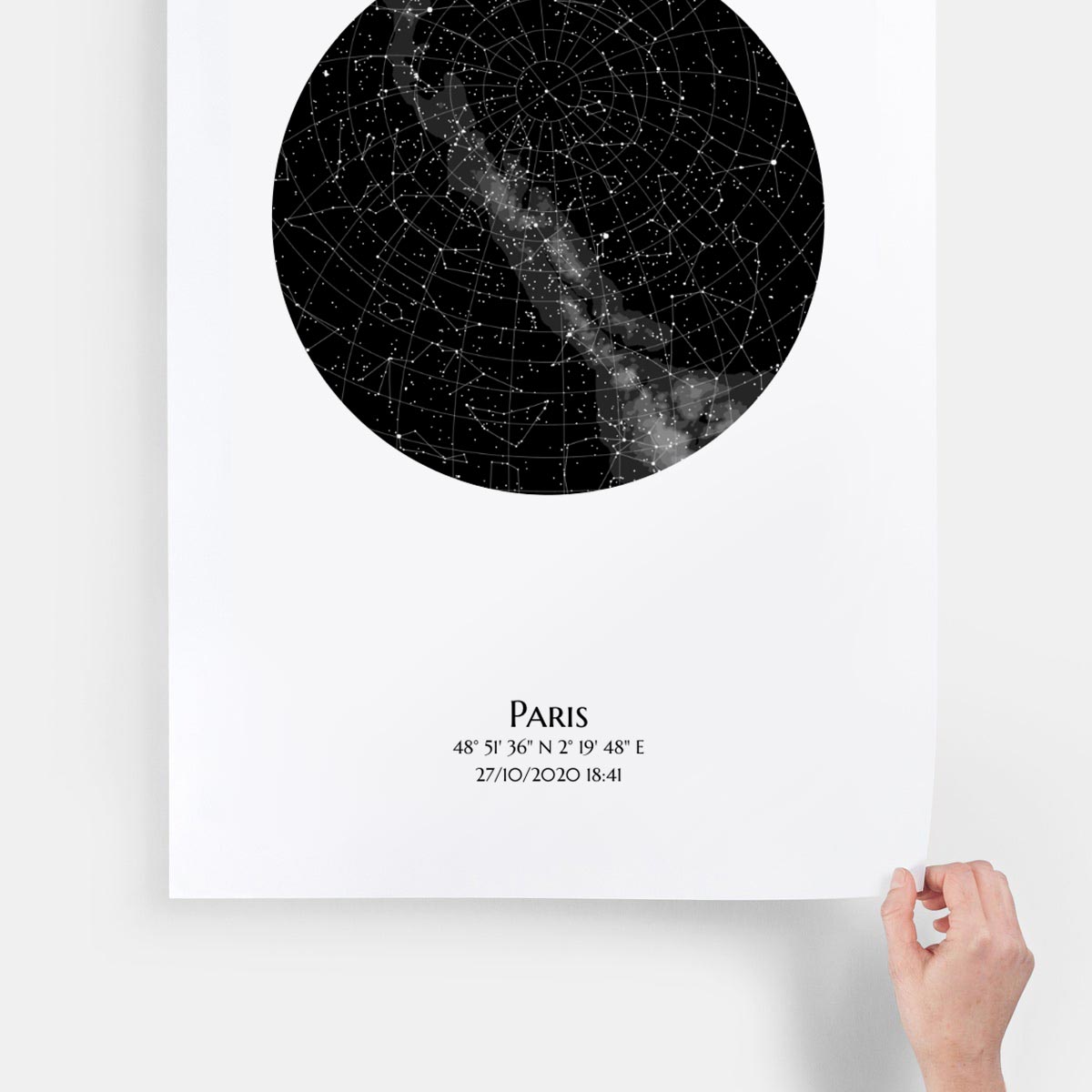 Poster premium luxe de Mundi représentant une carte des étoiles personnalisée pincé au coin par une main